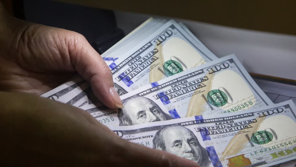 Рука тримає кілька купюр по 100 доларів США, видно частину серії банкнот